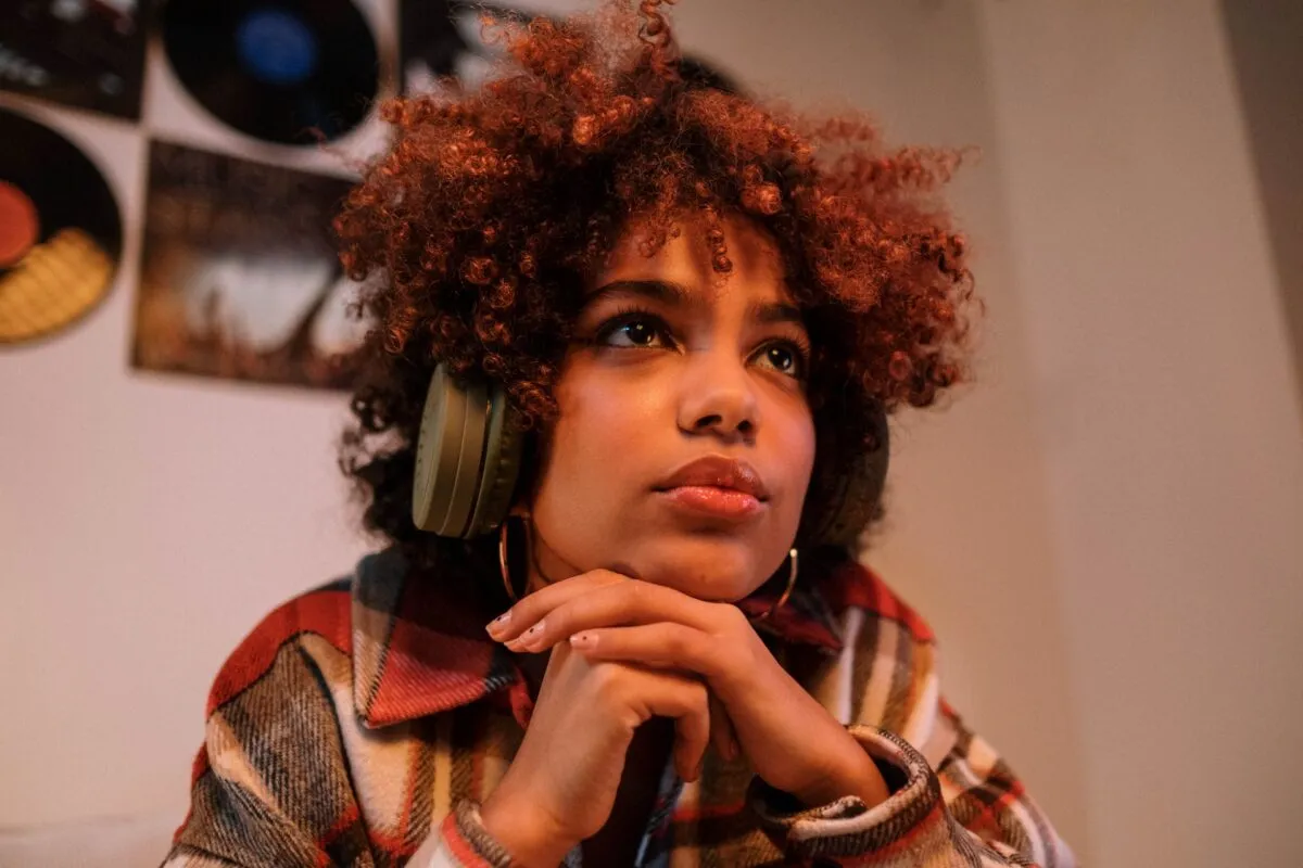 Mulher com fones de ouvido e expressão pensativa diante de uma parede com discos de vinil, ligando música a memória afetiva
